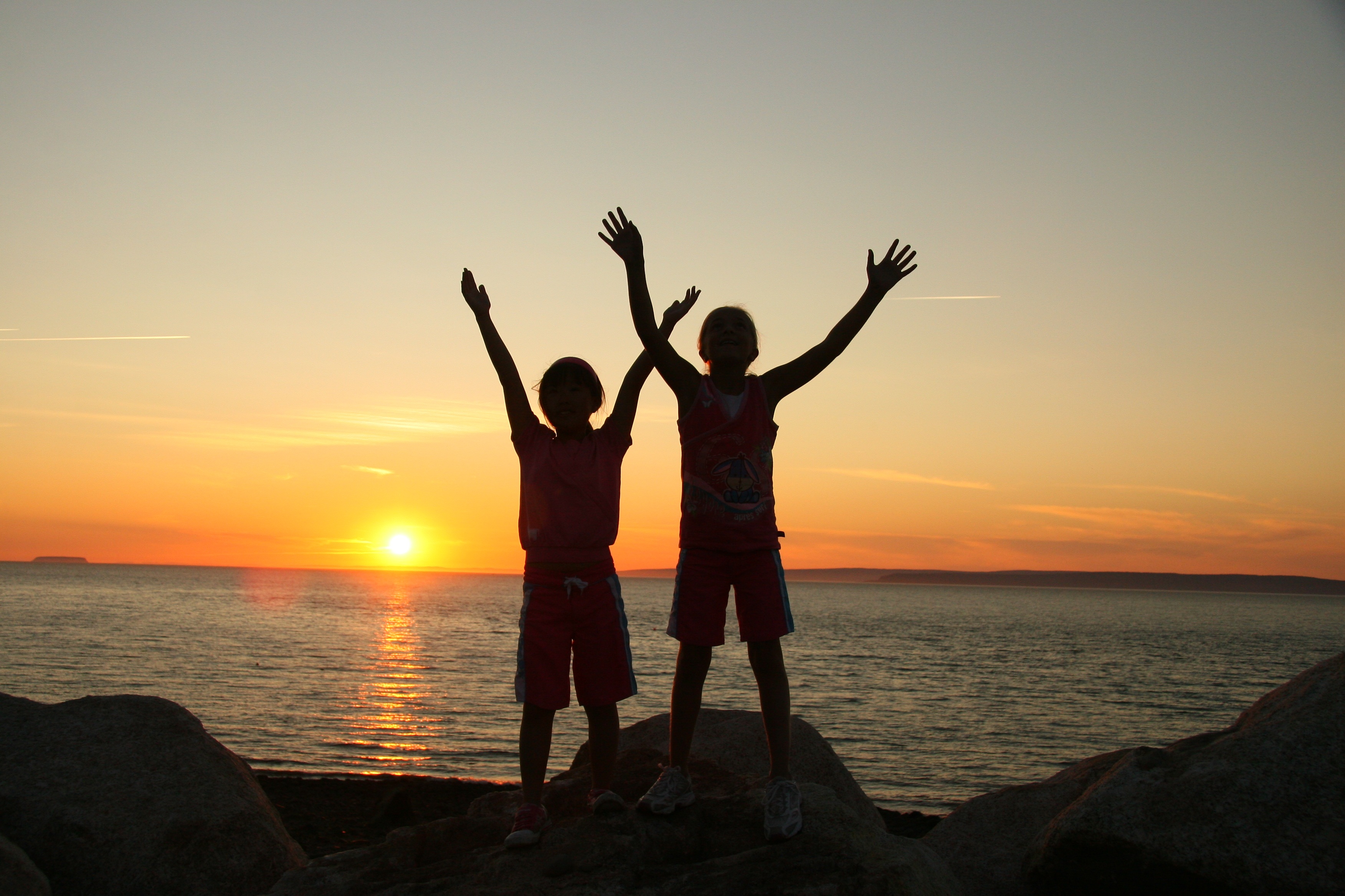 Silhouettes of two children in front of sunset over the ocean